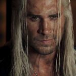 लियाम हेम्सवर्थ ‘The Witcher’ में Geralt के रूप में तलवार के साथ खड़े दिख रहे हैं, डार्क जंगल के बैकग्राउंड में।